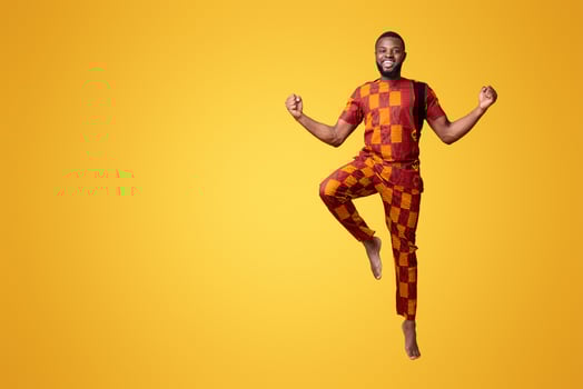 Excited black man in traditional clothes jumping up over yellow background photo