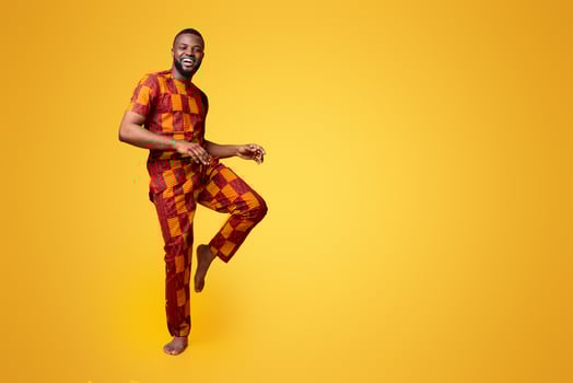 Charismatic black guy in traditional costume dancing over yellow background, having fun photo