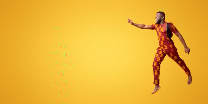 Excited black man in colorful authentic costume running towards copy space for advertisement, yellow background photo
