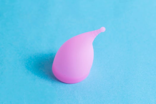 Pink female vaginal menstrual cup on a blue background, macro. Medical silicone bowl for girls for collecting discharge during menstruation photo