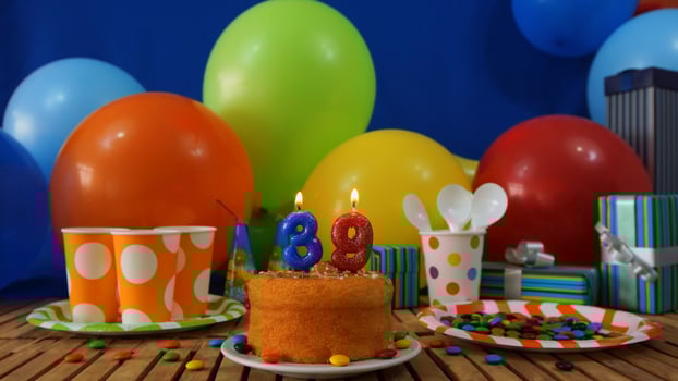 Birthday cake 39 on rustic wooden table with background of colorful balloons, gifts, plastic cups and plastic plate with candies and blue wall in the background photo