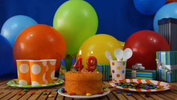 Birthday cake 49 on rustic wooden table with background of colorful balloons, gifts, plastic cups and plastic plate with candies and blue wall in the background photo