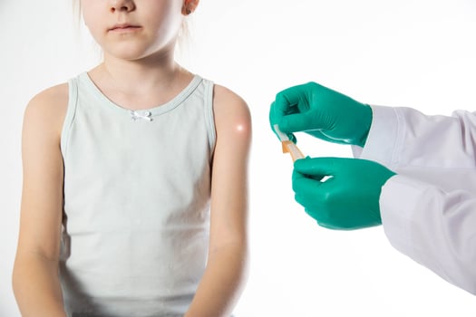 The hands of a doctor in green medical gloves hold a medical plaster against the background of a child s shoulder. Concept of vaccinations against tuberculosis and mumps for children. photo