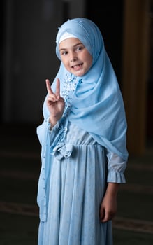 A happy Muslim child girl in hijab showing hand gesture v sign for victory or peace isolated portrait. photo