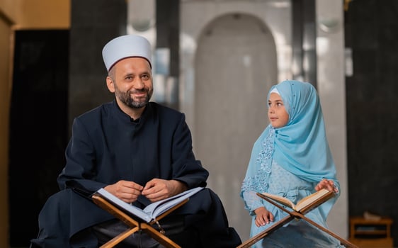 A Muslim teacher teaching child girl to reading a holy book Quran inside the Mosque Islamic people praying inside the masjid. photo
