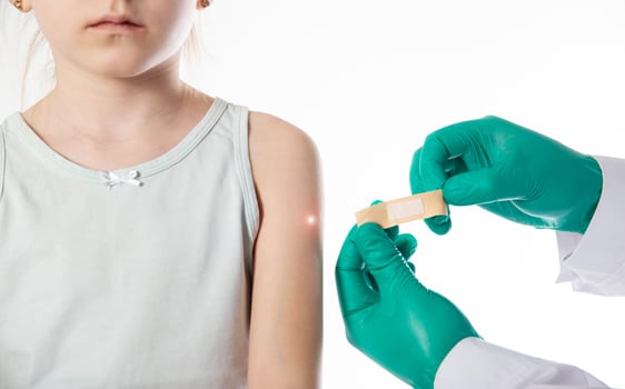 The hands of a doctor in green medical gloves hold a medical plaster against the background of a child s shoulder. Concept of vaccinations against tuberculosis and mumps for children. photo
