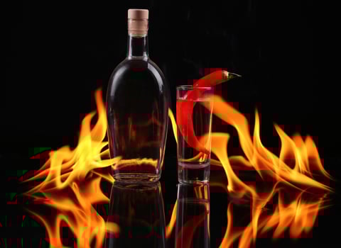 A bottle of vodka and a glass with a red pepper on fire photo