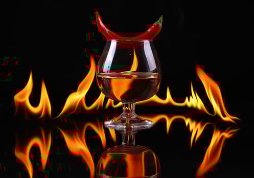Hot chili pepper in a cognac ballon with a fire on a black background photo