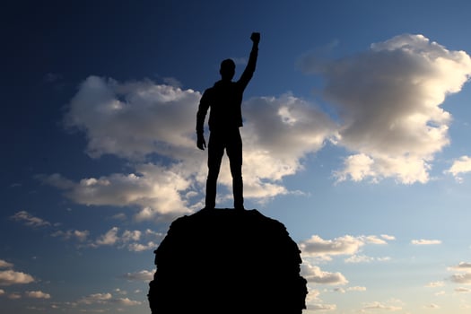 A man stands on top of a mountain with his hand raised photo
