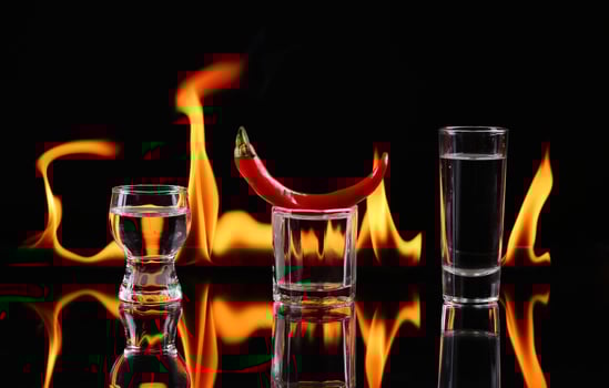A glass with a pepper and a shot glass on fire over dark photo