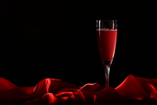 Glass of wine on red silk with dark background photo