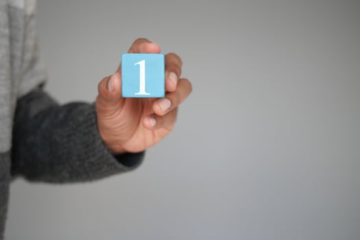 A hand is holding a blue block that has the number one inscribed on it against a neutral background photo
