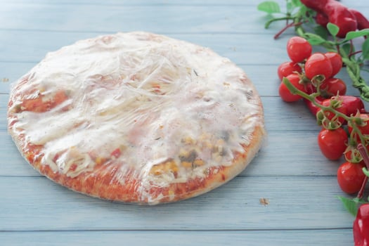 Frozen Pizza topped with Shrink Wrap and garnished with Fresh Cherry Tomatoes for flavor photo