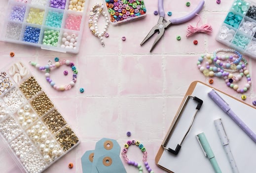 Colorful beads and jewelry making supplies arranged on pink tile background with clipboard and pens photo