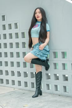 A woman in a blue shirt and boots leaning against a wall photo