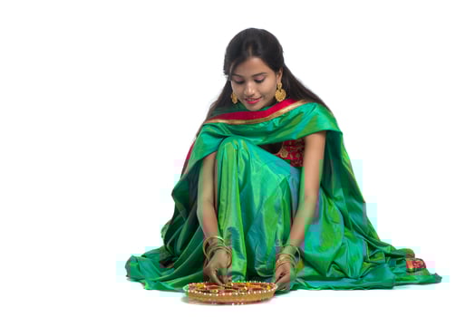 Portrait of a Indian Traditional Girl holding Diya and making Rangoli. Girl Celebrating Diwali or Deepavali with holding oil lamp during festival of light on white background photo