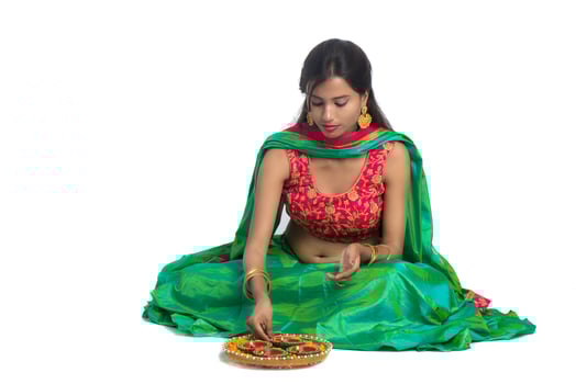 Portrait of a Indian Traditional Girl holding Diya and making Rangoli. Girl Celebrating Diwali or Deepavali with holding oil lamp during festival of light on white background photo