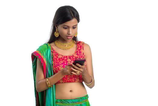 Young Indian traditional girl using a mobile phone or smartphone isolated on a white background photo