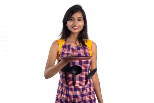 Young Indian woman holding kitchen utensil spoon, stapula, ladle, and pan, etc. on a white background photo