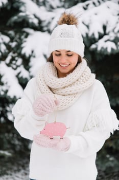 Girl in a white cap, sweater and mittens holding toy pig outside at winter snowy cold day, ready to celebrate new year and Christmas. photo