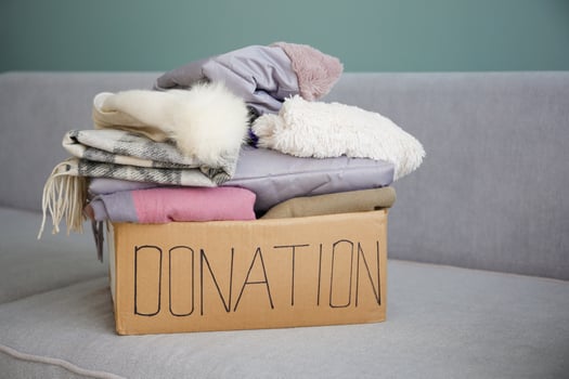 Donation box with clothes on a grey sofa in the living room. photo