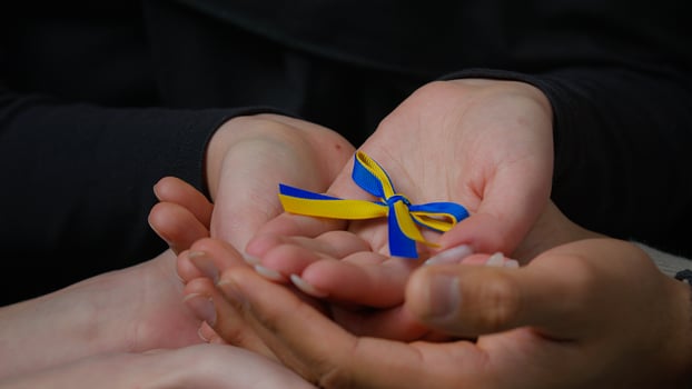 Close-up unrecognizable female and male hands hold blue yellow ribbon family couple volunteers palms holding ukrainian symbol stand with Ukraine protection charity support victims of war cropped view photo