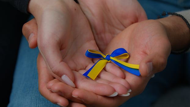 Close-up woman and man hands of multiracial family couple husband wife holding yellow blue colors ribbon national symbol Ukraine female male palms together support ukrainian people concept of charity photo
