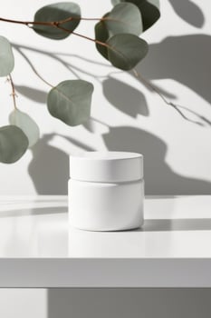 White cosmetic jar mockup casting a shadow on a white table with eucalyptus branches shadow background. photo