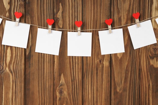 Clothespins with red hearts and empty sheets of paper on string against brown wooden background photo