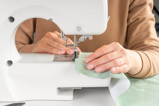 Tailor hands stitching green fabric on modern sewing machine at workplace in atelier photo