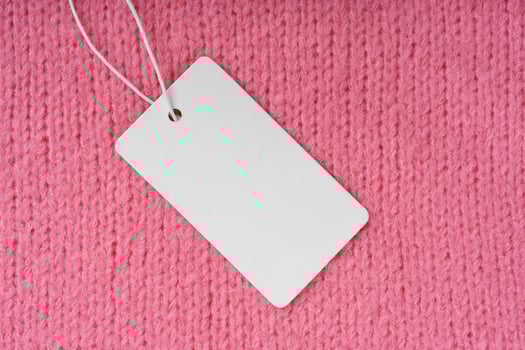 Template of blank clothing label, price tag on pink knitted sweater background photo
