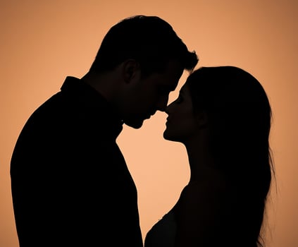 Couple embracing during sunset with silhouettes against orange sky photo