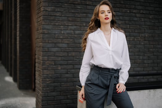 Businesswoman leaning against wall wearing white shirt and grey pants photo