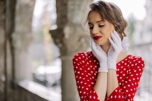 Elegant woman wearing white gloves and red polka dot dress posing in cloister photo