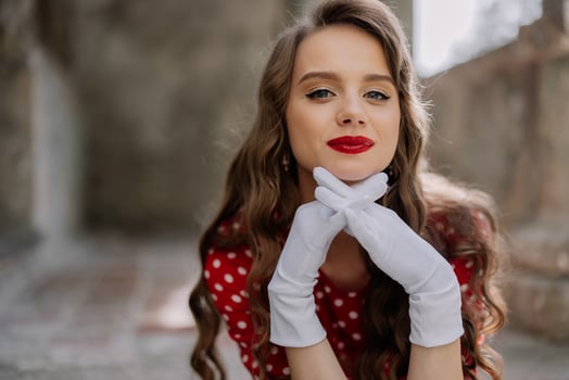 Elegant woman wearing white gloves and red polka dot dress posing in urban setting photo