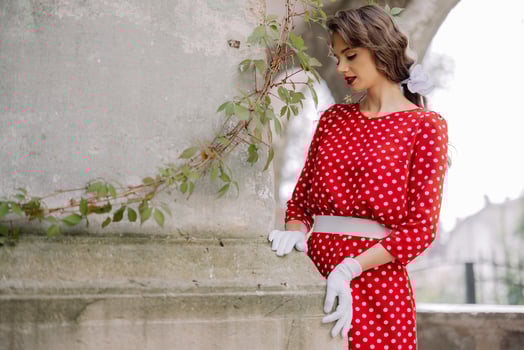 Elegant woman wearing red polka dot dress and white gloves posing by a stone column photo
