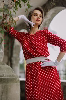 Elegant woman wearing red polka dot dress and white gloves posing in archway photo