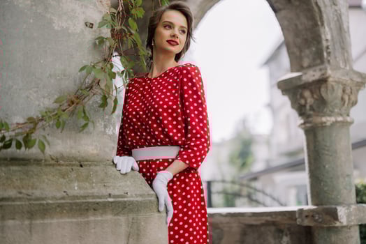 Elegant woman wearing red polka dot dress and white gloves posing in ancient ruins photo