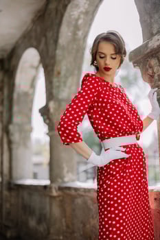 Elegant woman wearing red polka dot dress and white gloves posing in ancient ruins photo