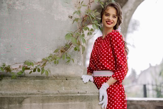 Elegant woman in red polka dot dress posing by stone column with ivy photo