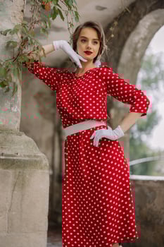 Elegant woman wearing red polka dot dress and white gloves posing in archway photo
