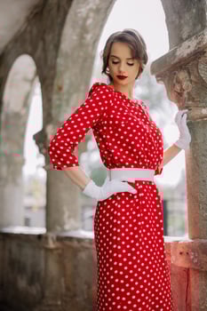 Elegant woman posing in red polka dot dress and white gloves near old building column photo