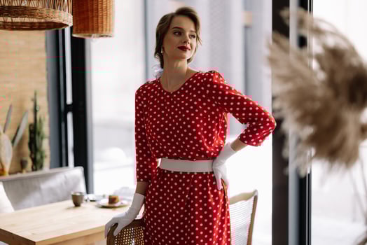 Elegant woman wearing red polka dot dress and white gloves posing in cafe photo