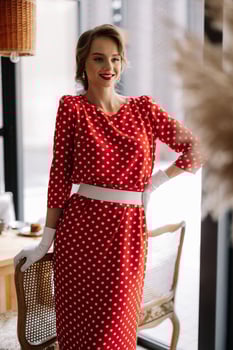 Elegant woman wearing red polka dot dress and white gloves posing in cafe photo