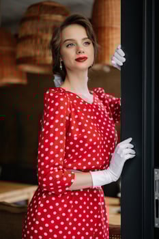 Elegant woman wearing red polka dot dress and white gloves opening a door photo