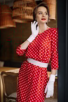 Elegant woman wearing red polka dot dress and white gloves posing in restaurant photo