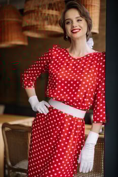 Elegant woman wearing red polka dot dress and white gloves posing in restaurant photo