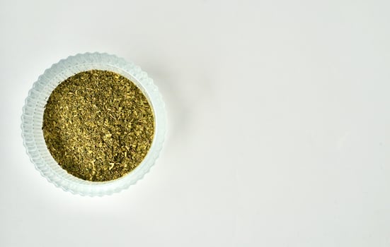 Dry ocha or green tea organic beverage leaves in round glass bowl container isolated on horizontal copy spaced white background. photo