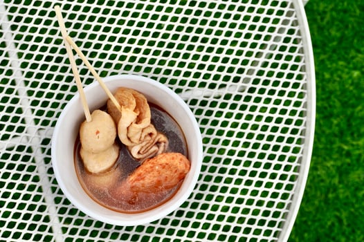 Oden fish cake food sticks with soup isolated on horizontal white table and green grass floor background from above top angle view. photo