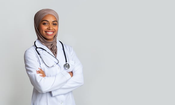 Medical Care For Muslim Women. Portrait Of Smiling Black Female Doctor In Hijab And White Coat Posing With Folded Arms Over Light Background, Panorama photo
